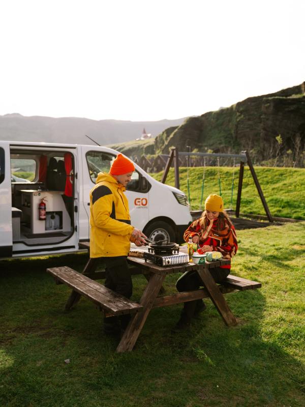 a man and a woman are sitting at a picnic table with a van in the background .