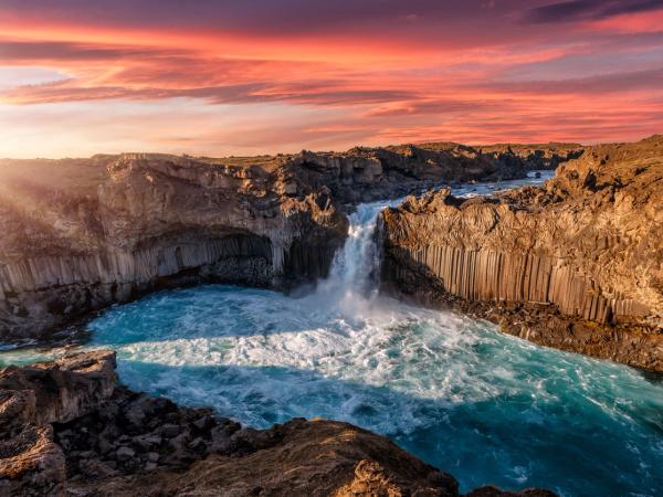 a waterfall in the middle of a canyon with a sunset in the background .