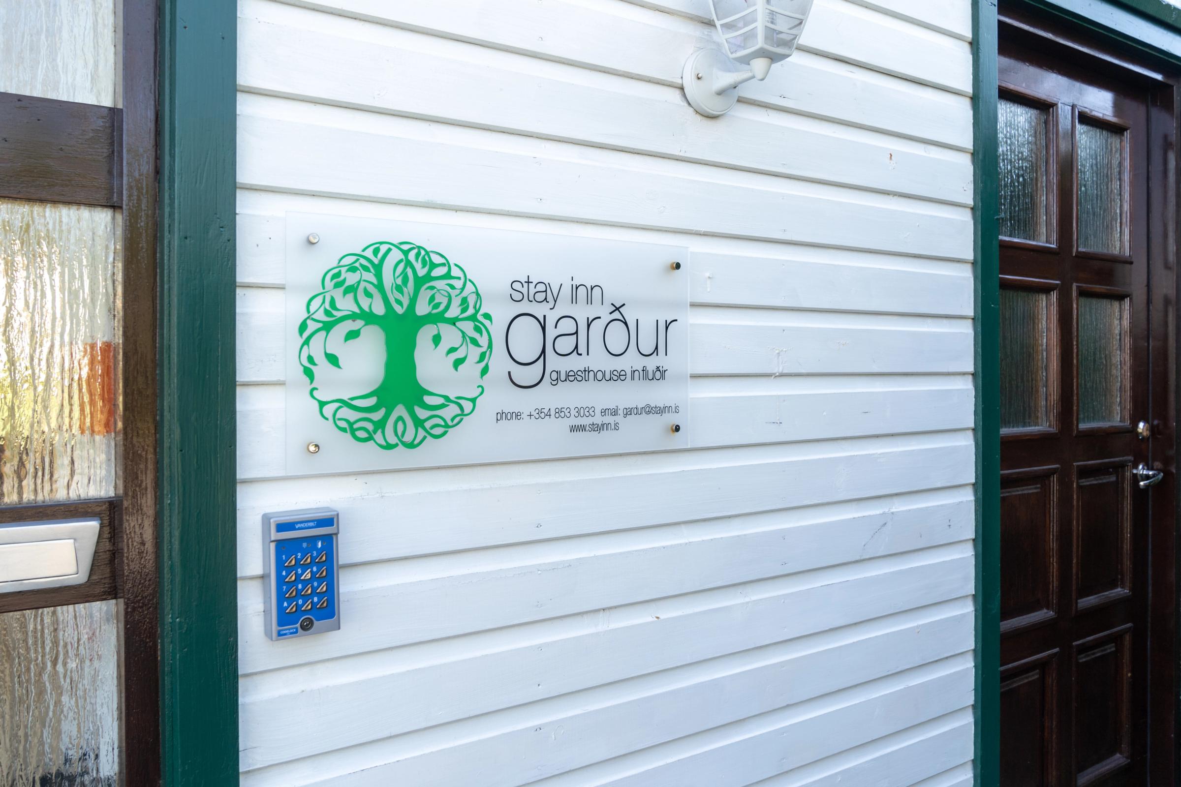 Letrero del Stay Inn Garður Guesthouse sobre un revestimiento blanco, junto a un sistema de entrada con tarjeta.