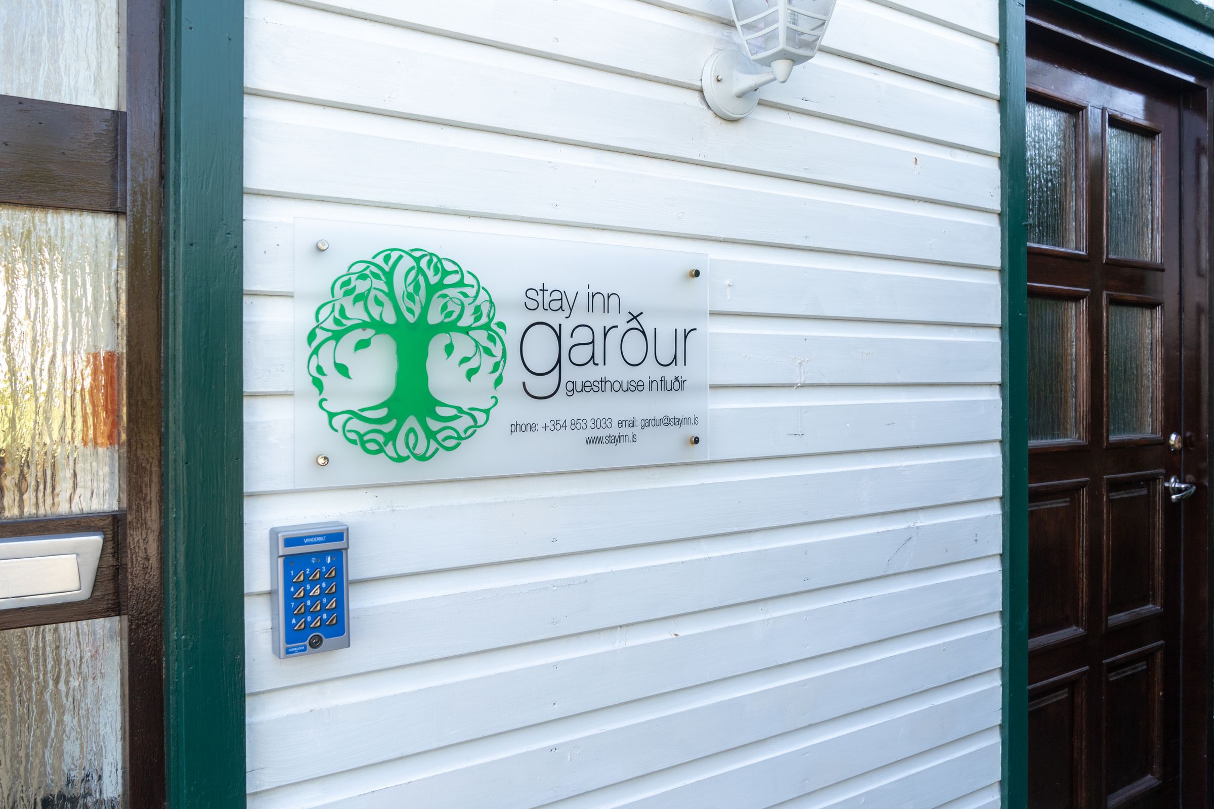Letrero del Stay Inn Garður Guesthouse sobre un revestimiento blanco, junto a un sistema de entrada con tarjeta.