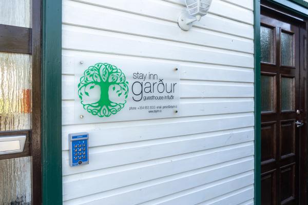 Sign for Stay Inn Garður Guesthouse on white siding with a keycard entry system.