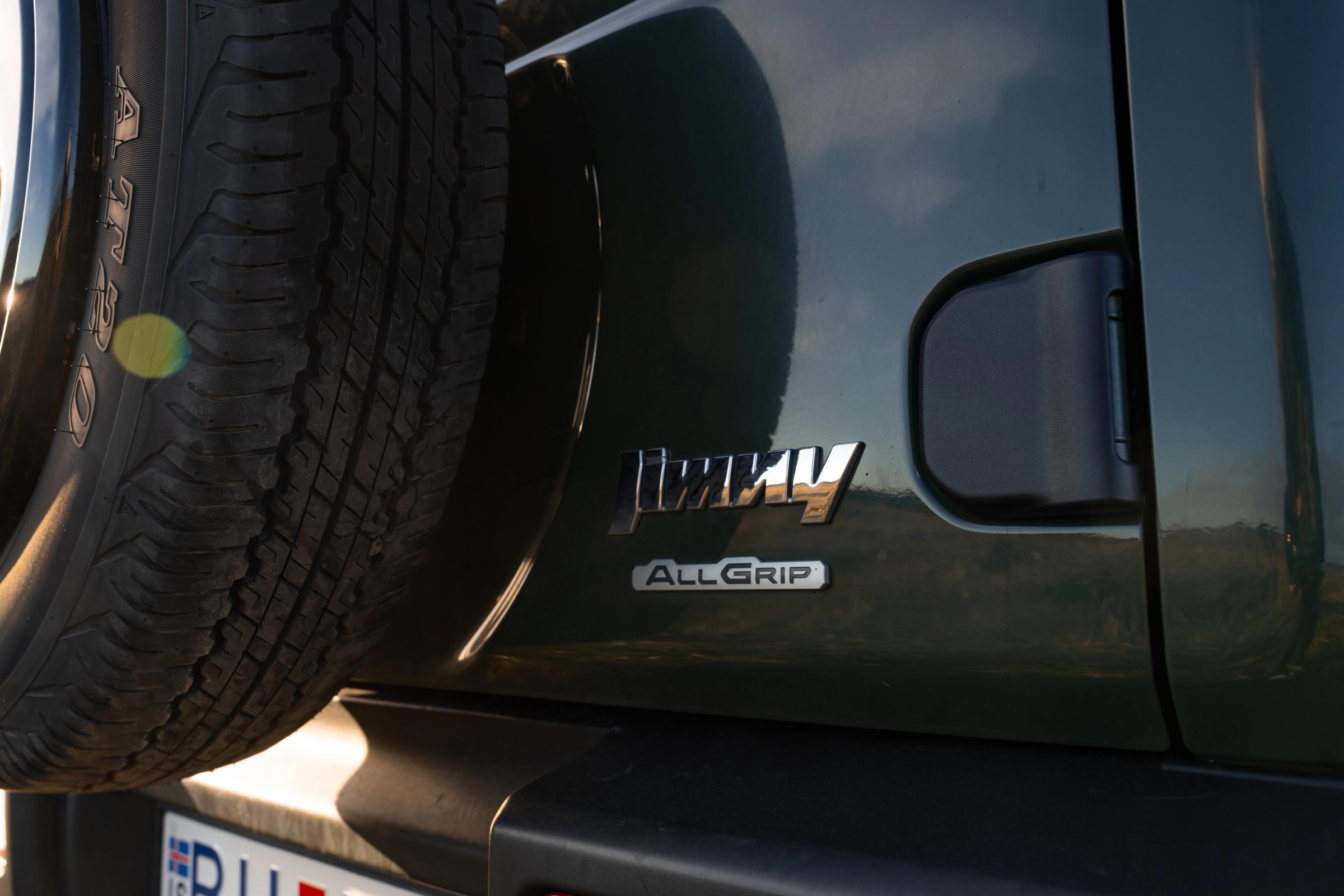 Nahaufnahme des Hecks eines Suzuki Jimny mit Schaltgetriebe, Modellschriftzug, AllGrip-Emblem und Reserverad