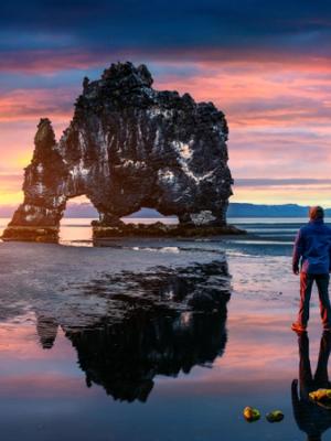 a man is standing on a beach looking at the Elephant Rock in Iceland