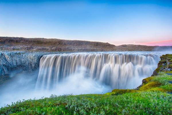 a waterfall in the middle of a field with a blue sky in the background at dettifoss in north Iceland.
