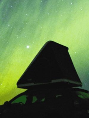 Coche con una tienda de campaña en el techo bajo la aurora boreal