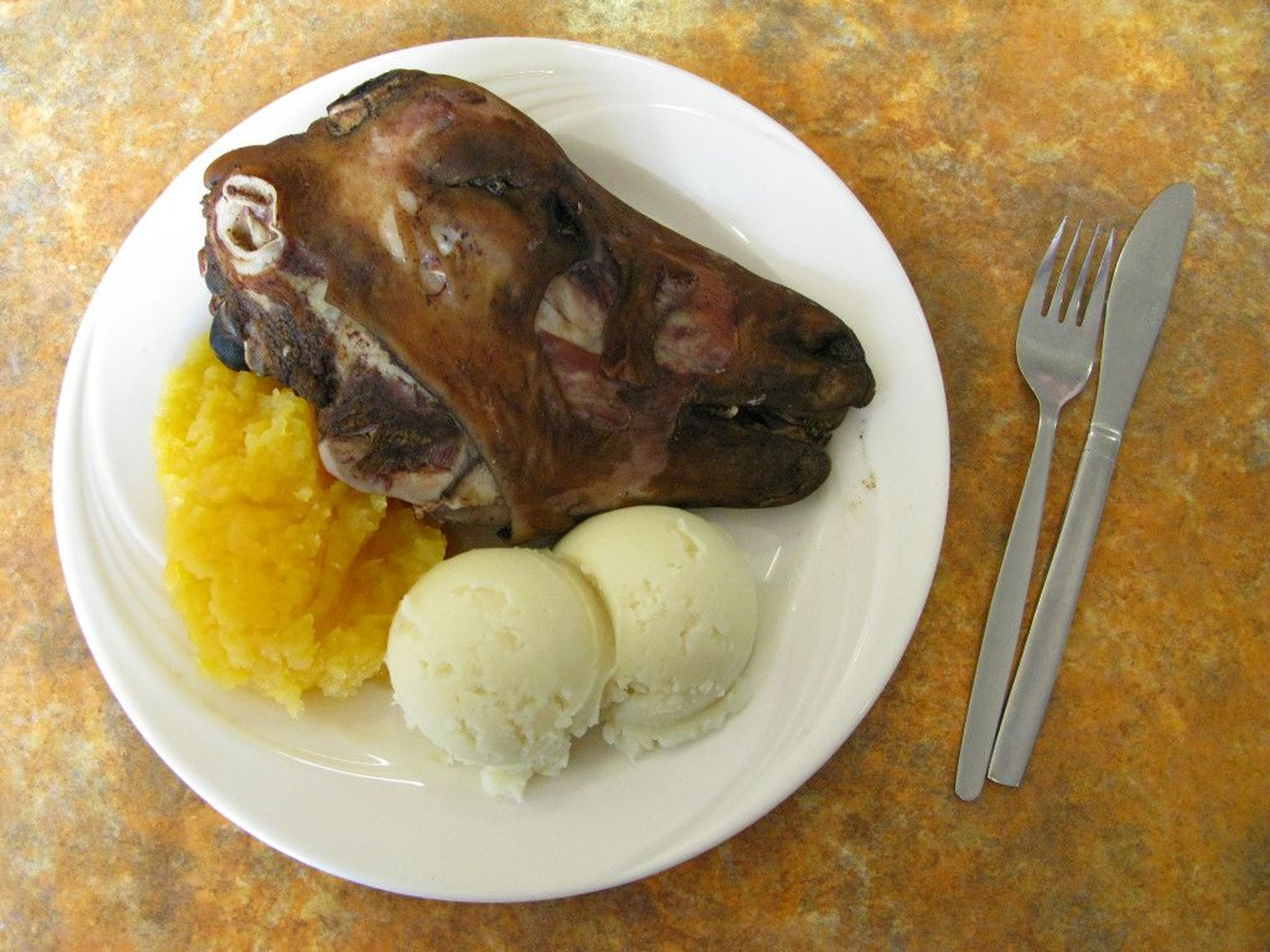 Cooked sheep's head, yellow mash, and potatoes on a plate with cutlery.