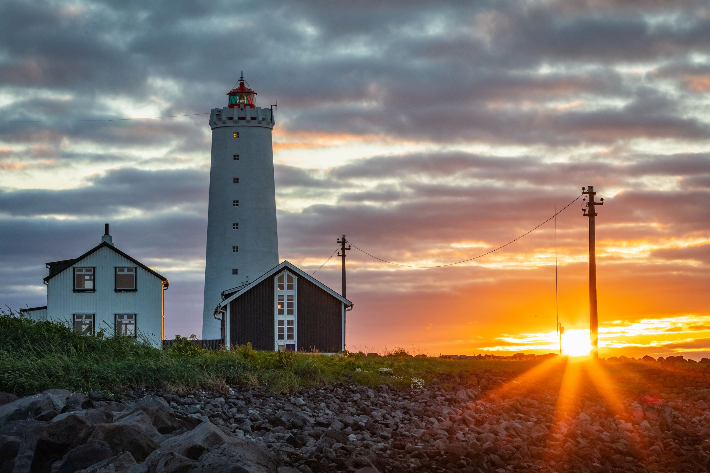 A white lighthouse with two houses next to it during sunset