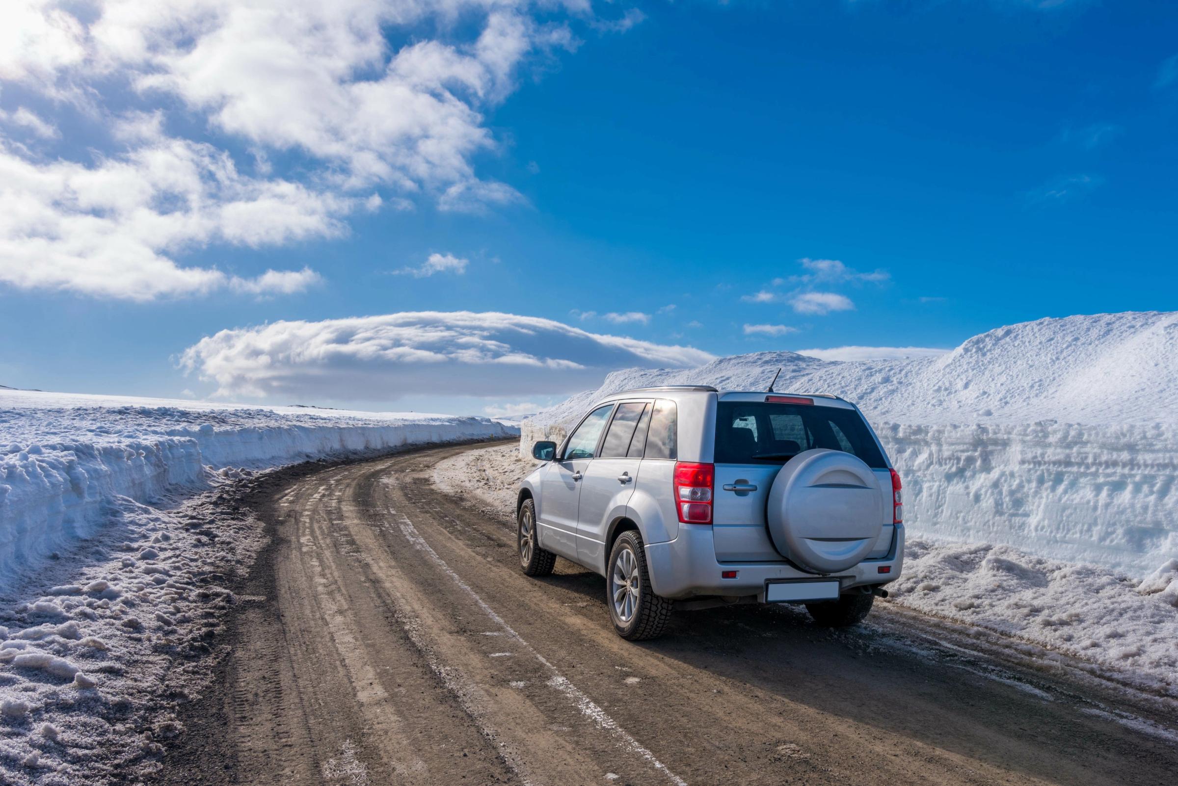 SUV plateado en un camino de tierra entre grandes bancos de nieve bajo un cielo azul y nublado.