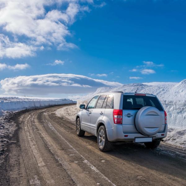SUV plateado en un camino de tierra entre grandes bancos de nieve bajo un cielo azul y nublado.