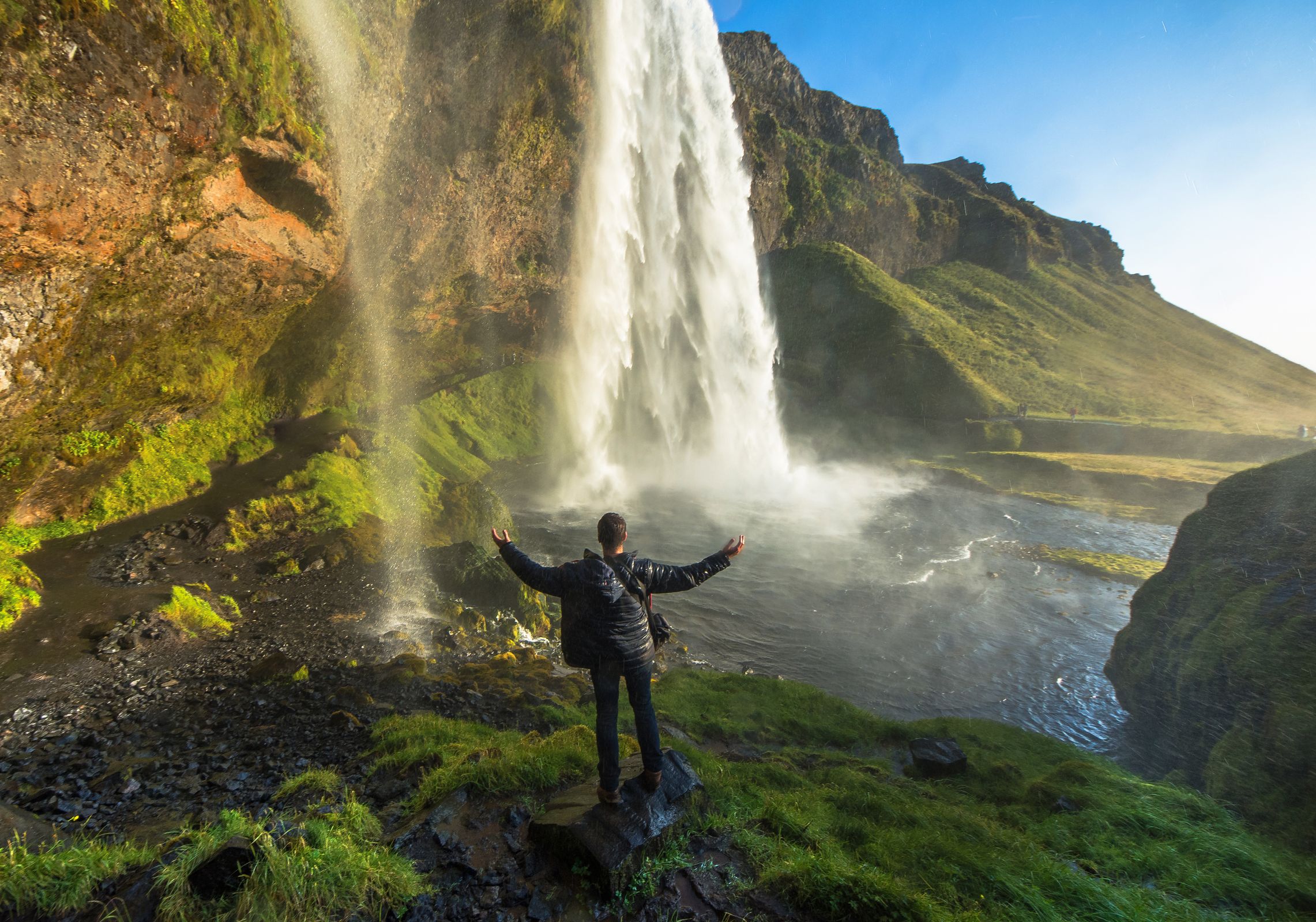 a man is standing in front of a waterfall with his arms outstretched .