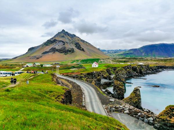 a road going through a grassy field next to a body of water with a mountain in the background .
