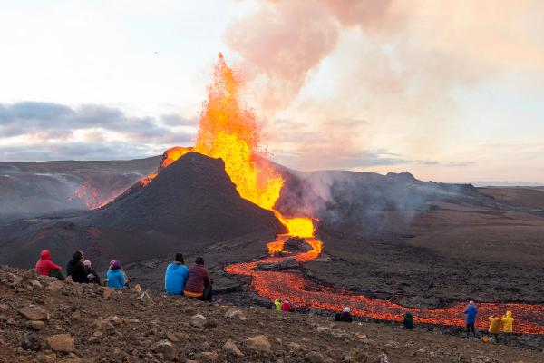 a group of people are sitting on top of a hill watching a volcano erupt, Geldingadalir