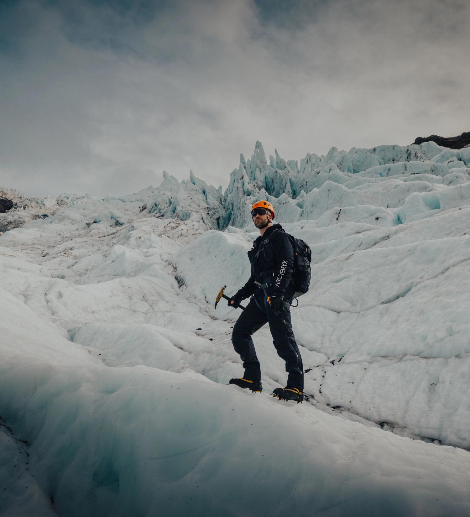 A person wearing a helmet and carrying an ice axe walks across a glacier.
