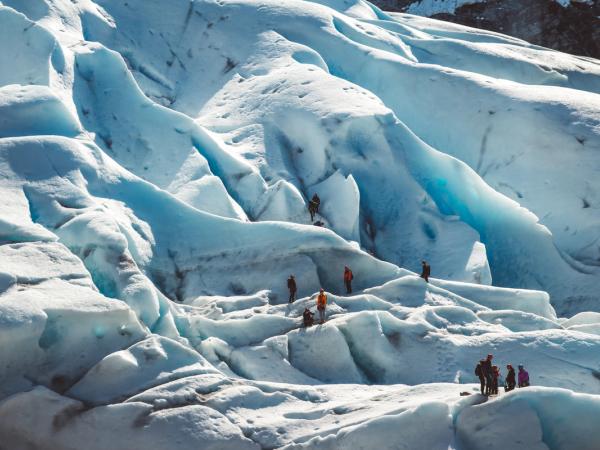 Hikers traverse a rugged blue and white glacier.