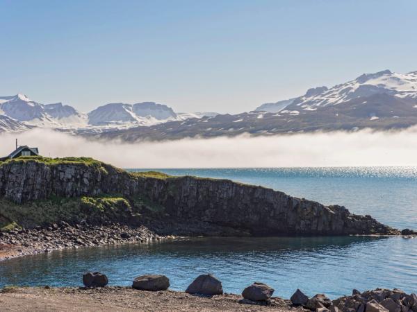 a small house on a rocky cliff overlooking a lake with mountains in the background .