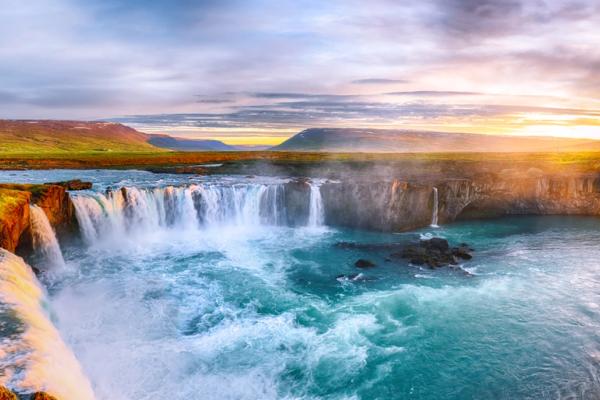 a waterfall in the middle of a river at sunset .