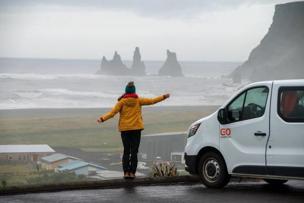 a woman is standing on a wall next to a van looking at the ocean .