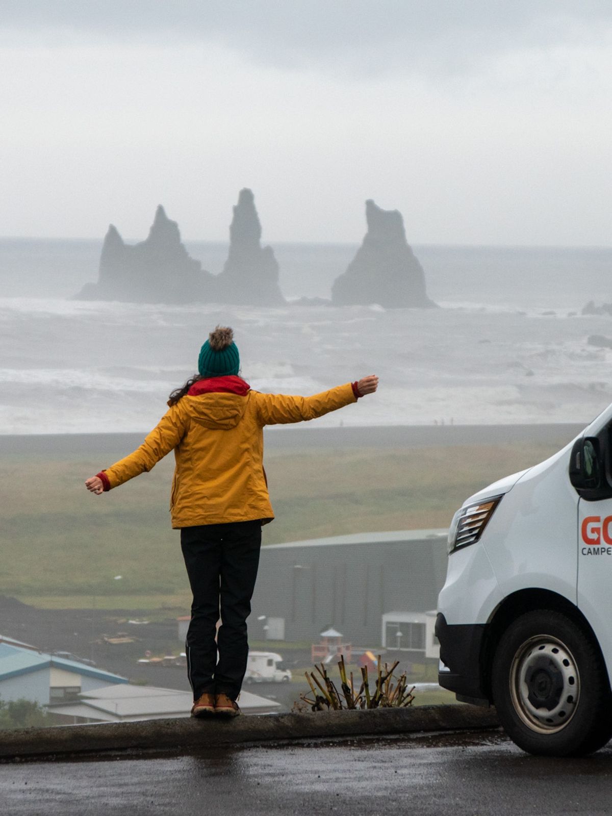 a woman is standing on a wall next to a van looking at the ocean .