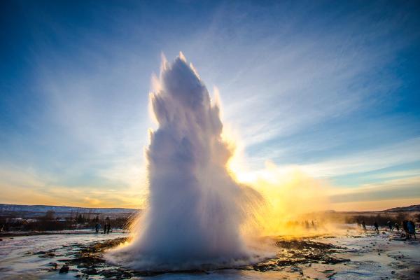 a large geyser is erupting into the air at sunset .