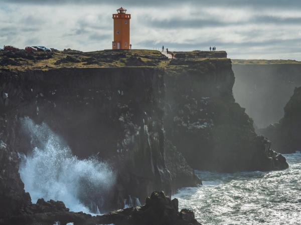 un faro en la cima de un acantilado con vistas al océano y olas rompiendo contra las rocas.
