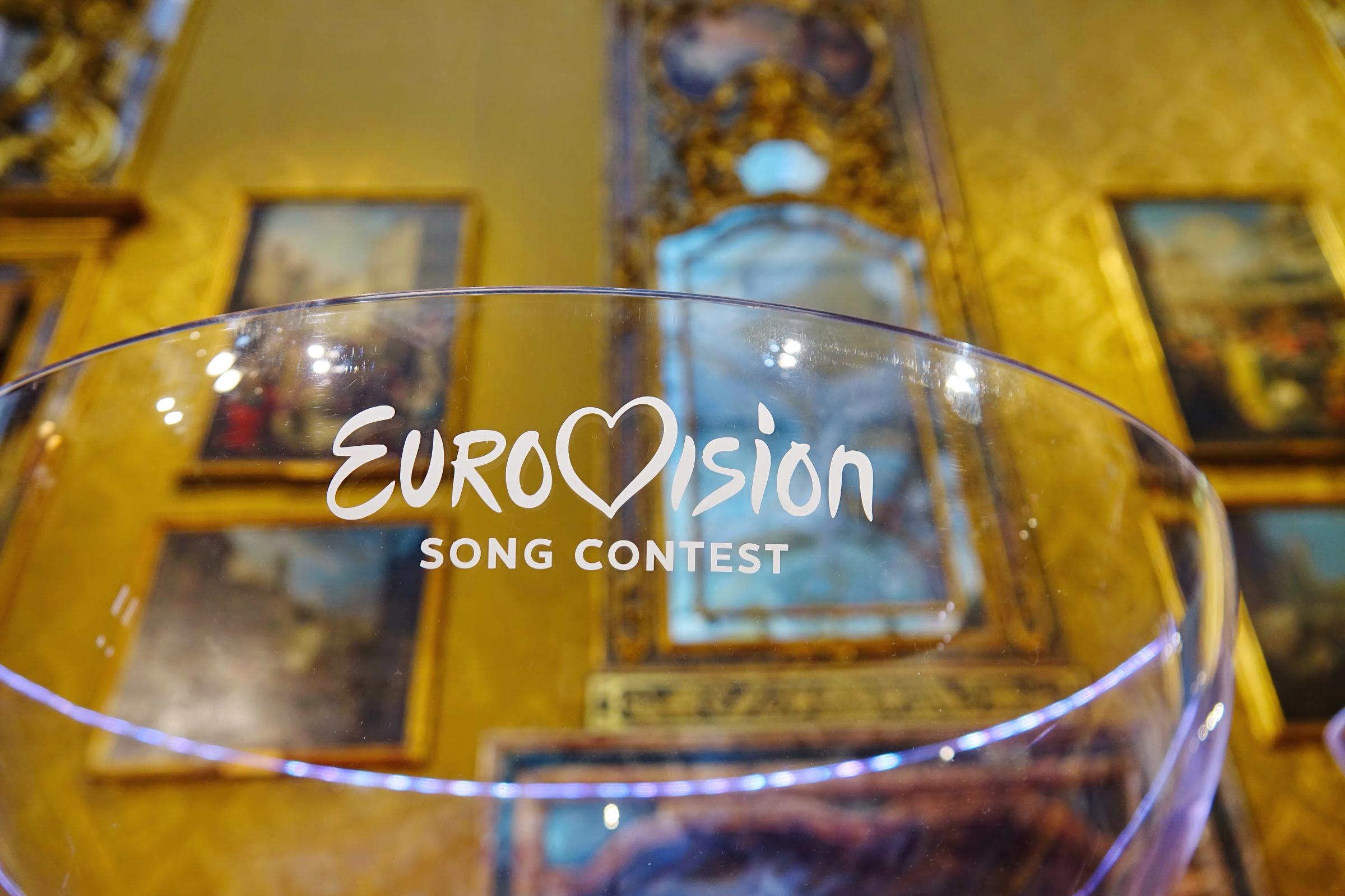un vaso con las palabras eurovision song contest escritas en él está situado frente a una pared con pinturas.