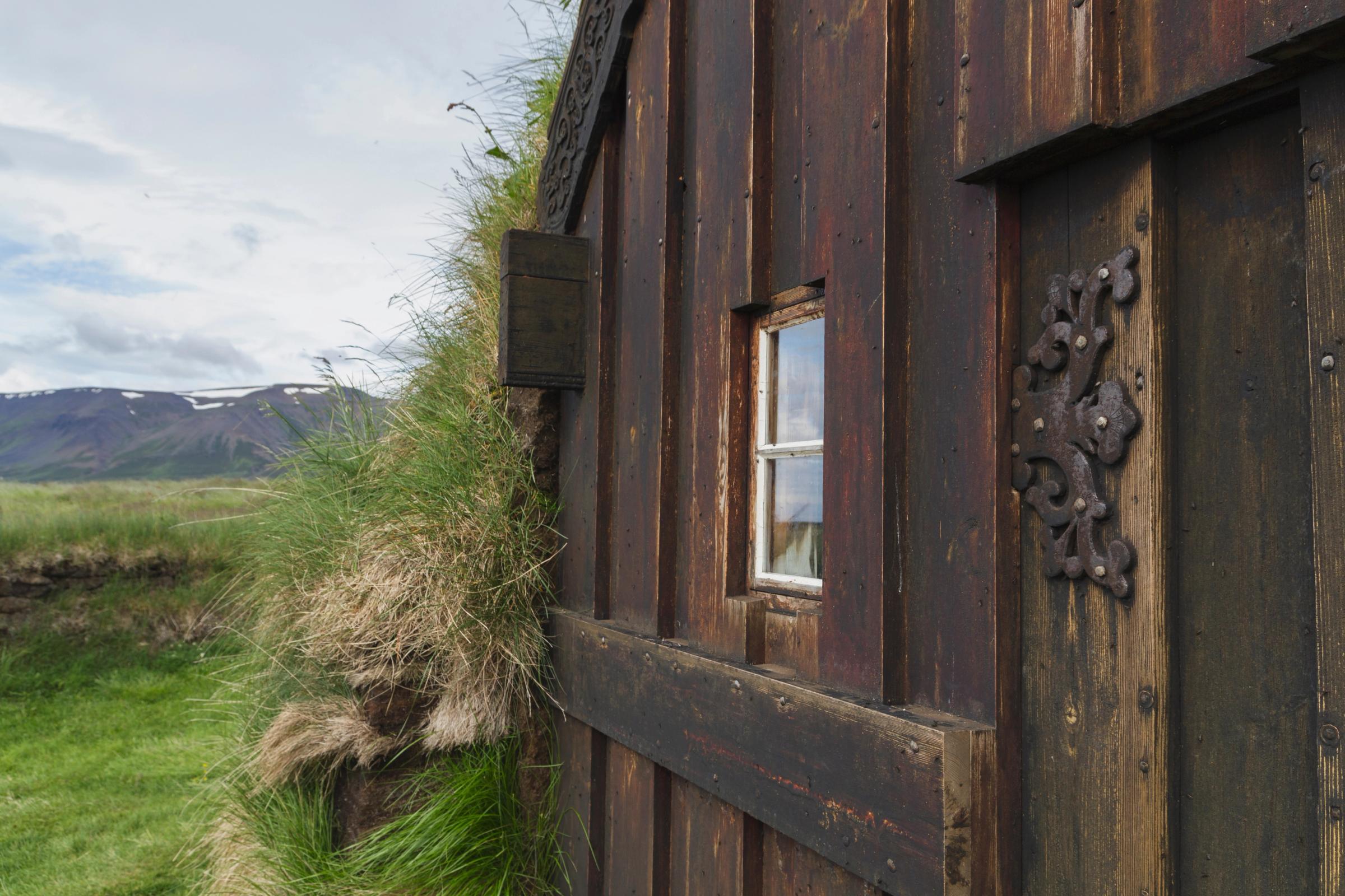 a wooden building with a window in the middle of a grassy field .