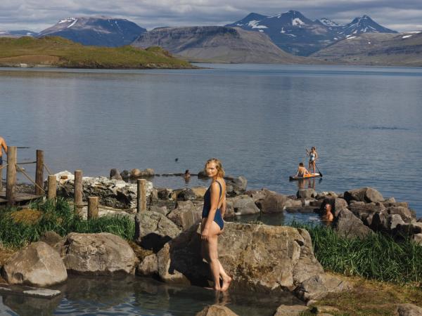 Mujer posando en Hvammsvík con el lago, las montañas y gente detrás de ella