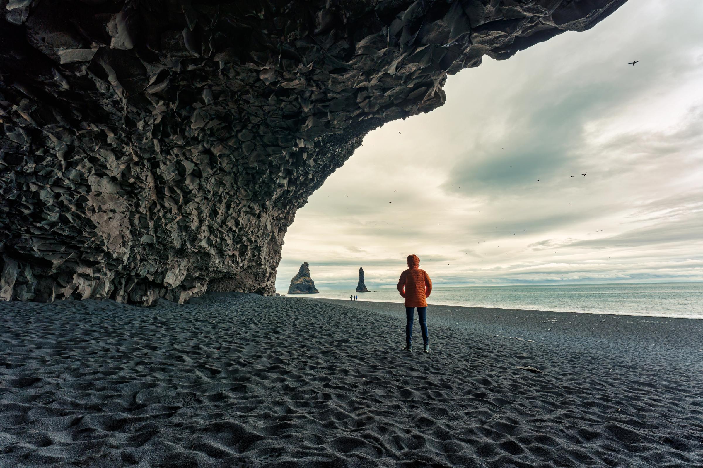 Hombre debajo de una cueva en una playa de arena negra
