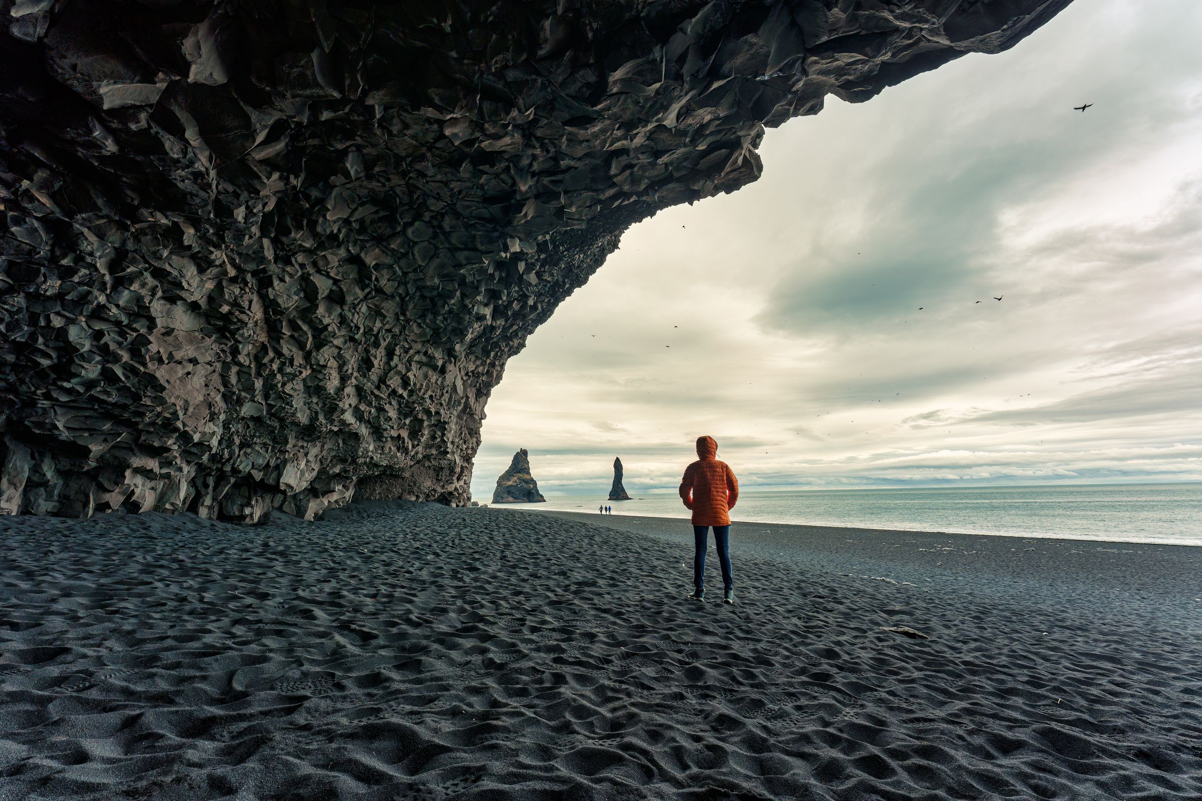 Hombre debajo de una cueva en una playa de arena negra