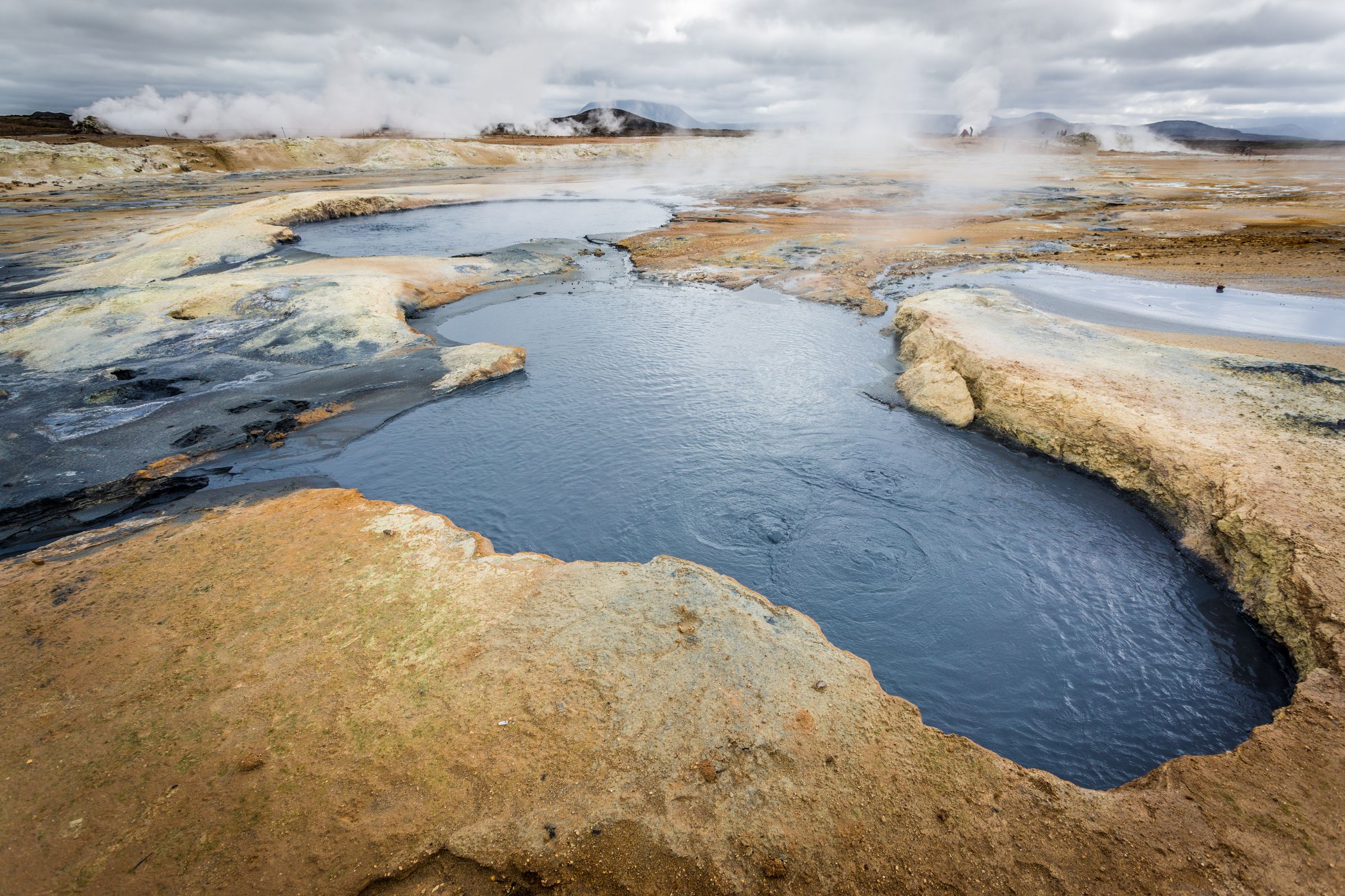 a large body of water surrounded by rocks and dirt with steam coming out of it at hverir near lake mývatn in iceland.