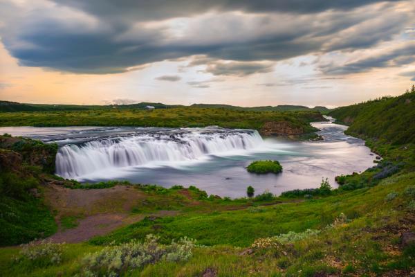 there is a waterfall in the middle of a river in the middle of a field at Faxafoss in Iceland.