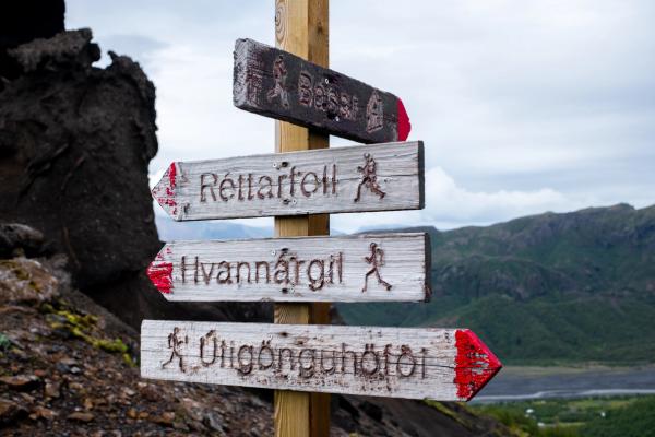 A weathered wooden signpost with multiple directional signs for hiking trails in a rugged mountainous landscape.