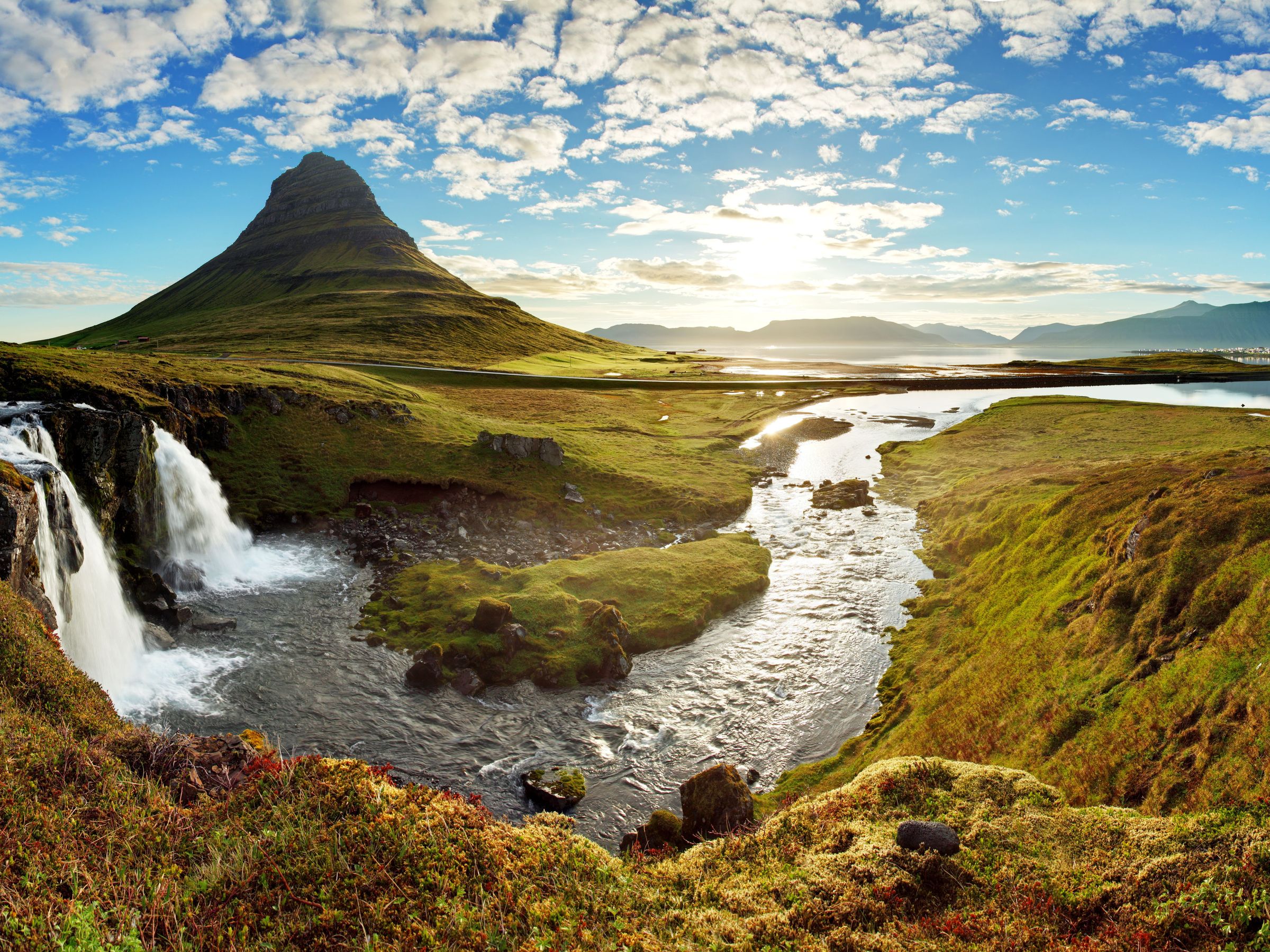 Kirkjufellsfoss Waterfall on a sunny day with Kirkjufell mountain in the background