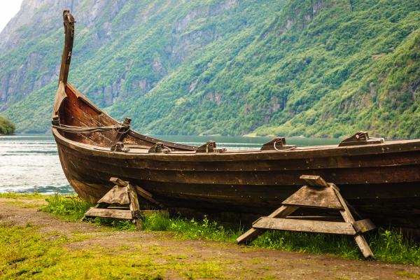 an old wooden viking boat is sitting on the shore of a lake .