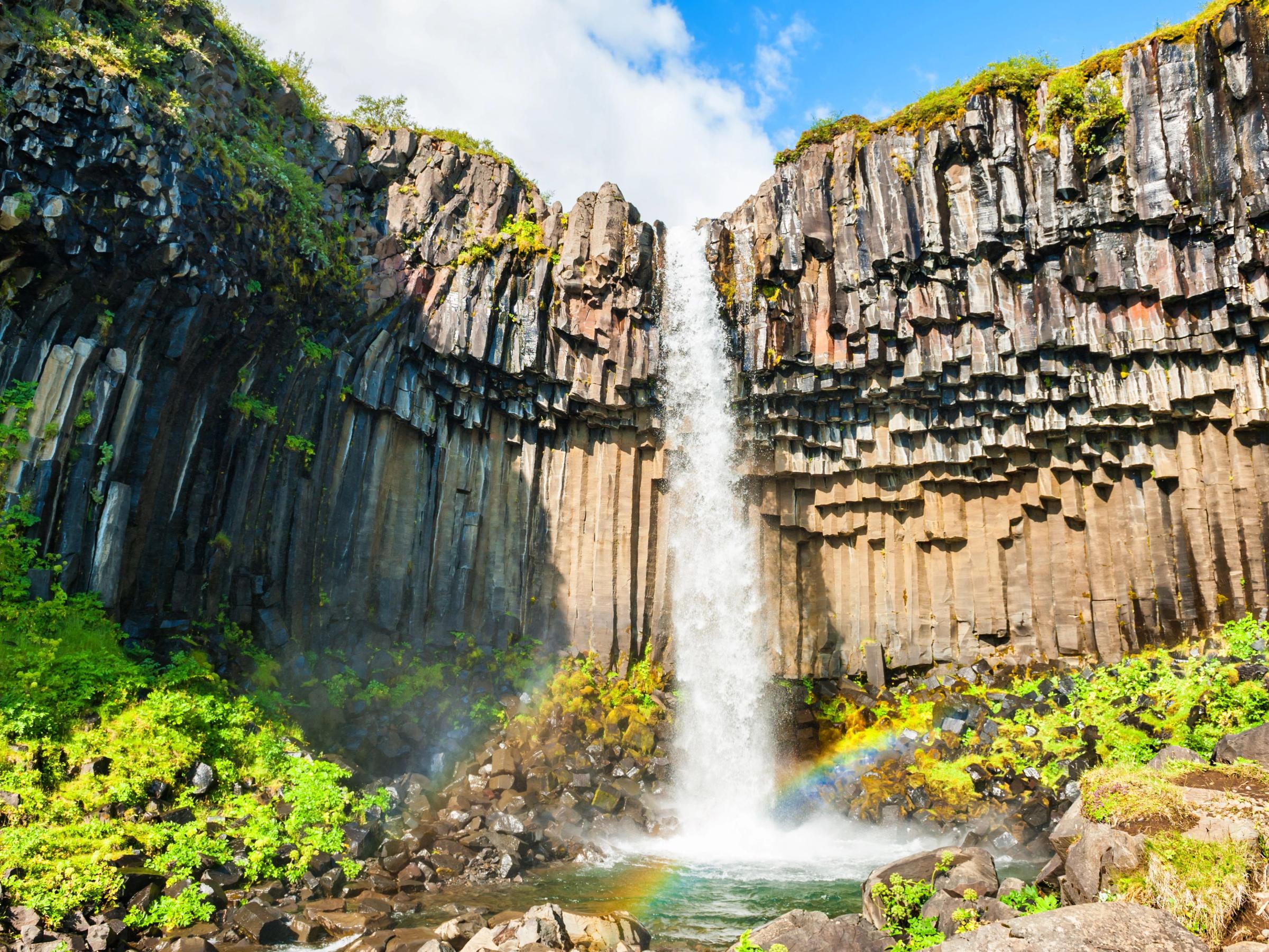 Svartifoss en un día soleado con un arcoiris en frente