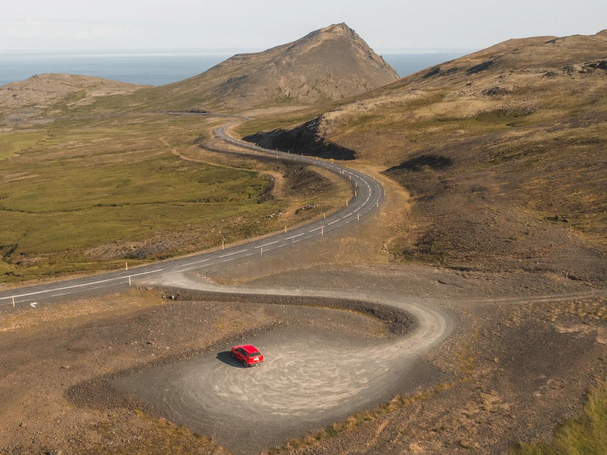 Vitara sur une route aérienne sinueuse Petite Suzuki Vitara rouge sur une route goudronnée sinueuse, avec le littoral au loin, autotour en Islande