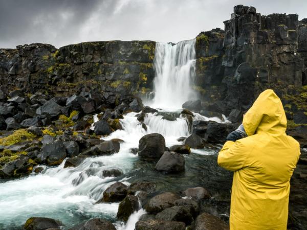 Man wearing a yellow raincoat photographing a waterfall