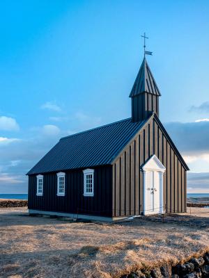 a small black church with a cross on top of it is sitting on top of a hill next to the ocean .