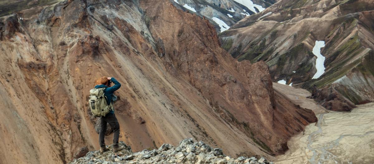a man with a backpack is standing on top of a mountain looking through binoculars. Hiking in iceland.