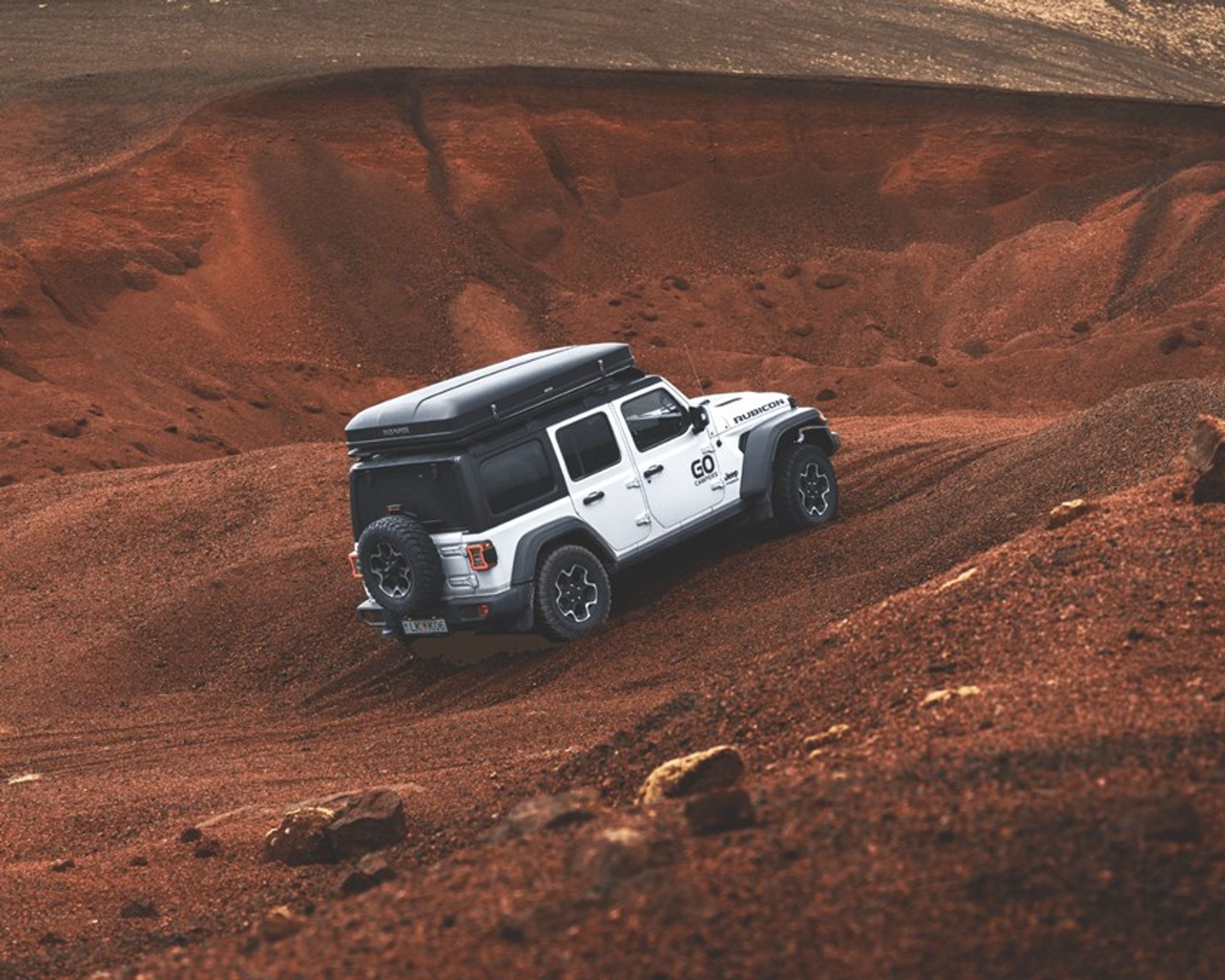 Jeep Wrangler blanco con tienda de techo subiendo una empinada colina todoterreno de color marrón rojizo.
