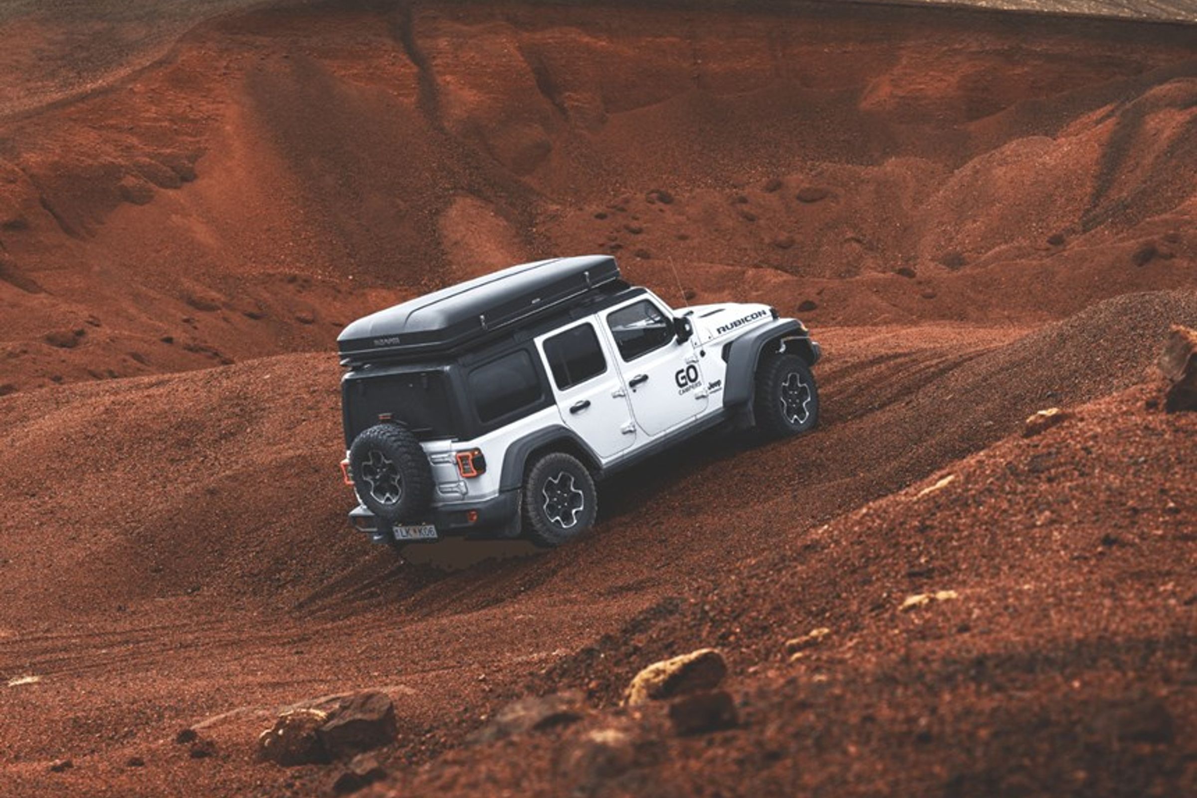 Jeep Wrangler blanco con tienda de techo subiendo una empinada colina todoterreno de color marrón rojizo.