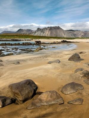 a sandy beach with rocks and mountains in the background .