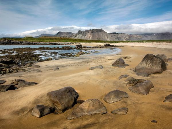 una playa arenosa con rocas y montañas al fondo.