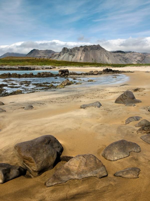 una playa arenosa con rocas y montañas al fondo.