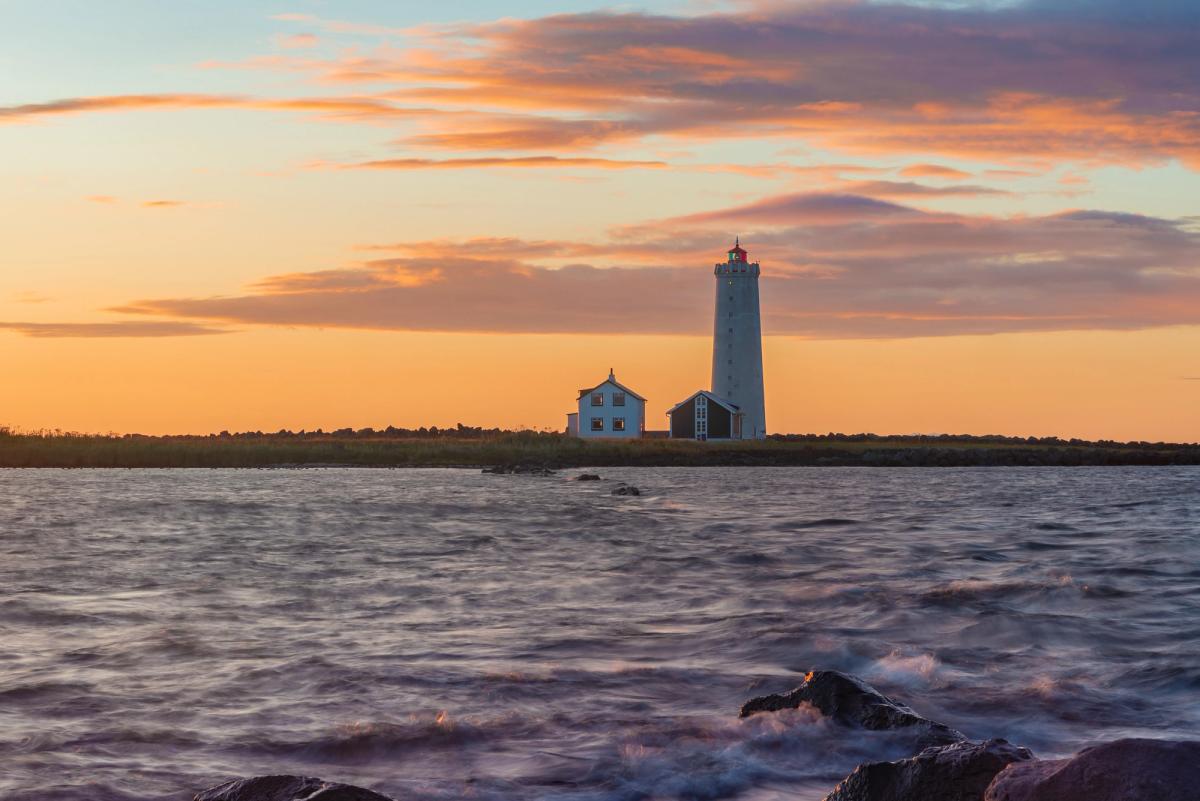 A white lighthouse near the sea with two houses next to it during sunset