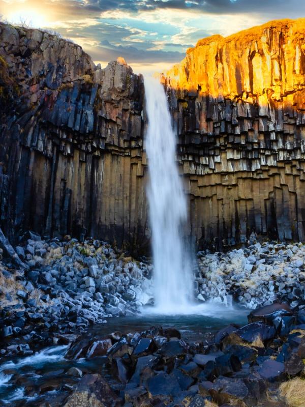 Vista de Svartifoss al atardecer con un rayo de luz alumbrando una parte de las columnas de balsalto