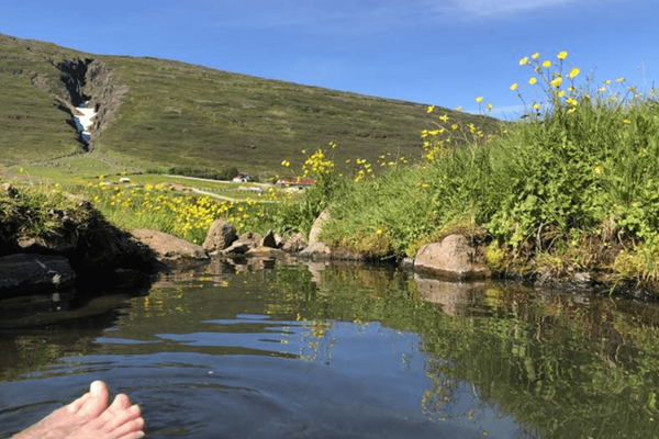 a person 's feet are sticking out of a body of water at Heydalur in iceland.