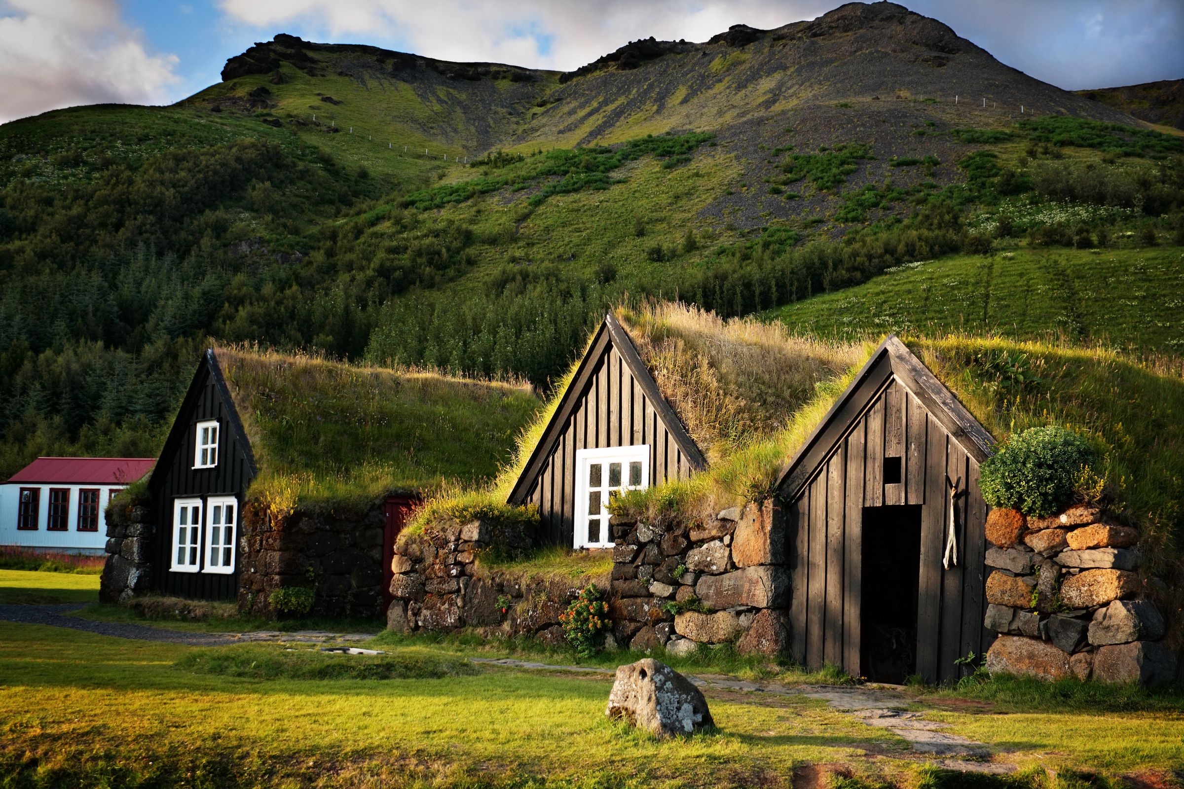 Three traditional turf-roofed houses with wooden facades in a lush green landscape.