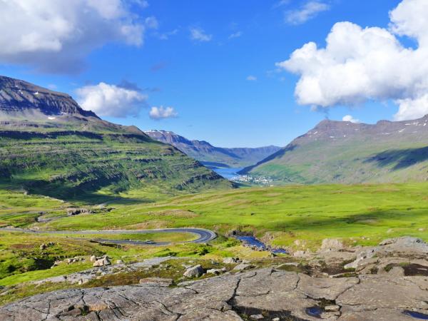 a road winds through a lush green valley surrounded by mountains .
