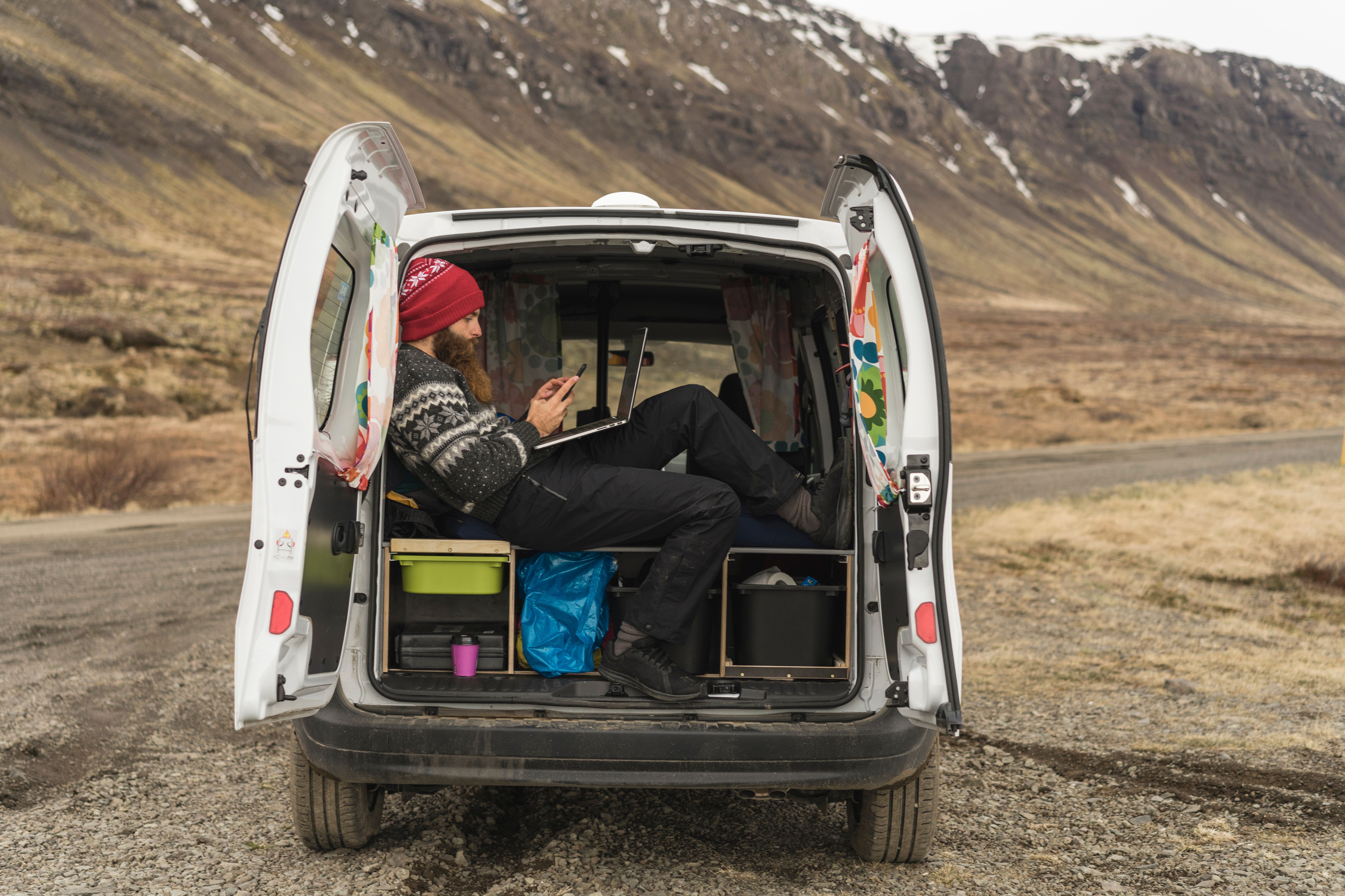 a man is sitting in the back of a campervan in iceland looking at his phone .